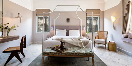 Spacious guestroom with pale walls, canopy bed, and bench seating in a calm, minimalist style.
