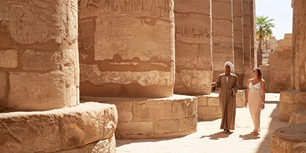Guests walking through a monumental temple complex in Egypt, guided through sunlit courtyards lined with carved stone pillars.