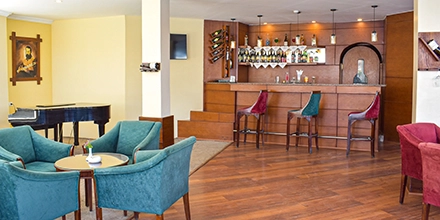 A cosy bar lounge with velvet armchairs, warm timber floors and a well-stocked counter set beneath soft lighting.