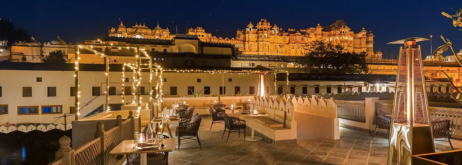 Rooftop terrace dining setup overlooking Udaipur’s illuminated City Palace at night