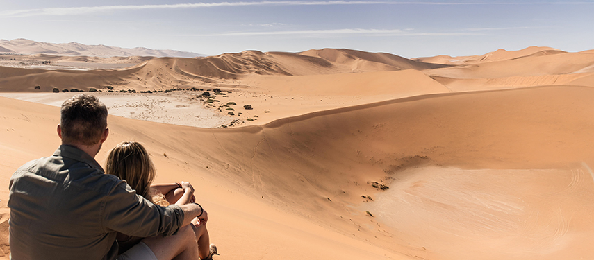 Couple sit on top of a dune admiring the view in Namibia