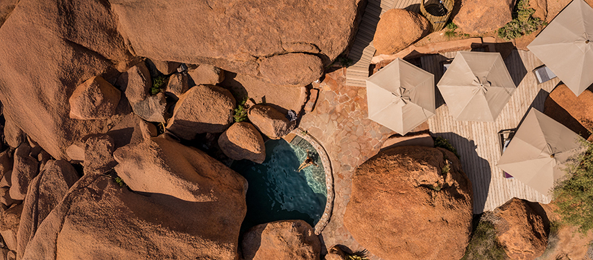 Drone view of a woman swimming in a private pool amongst the huge red rocks of Namibia's Damaraland