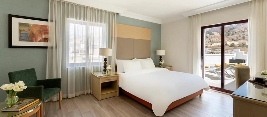 A bright and contemporary guest room at Mövenpick Hotel Petra opens onto a private terrace with views across the rugged Petra landscape.
