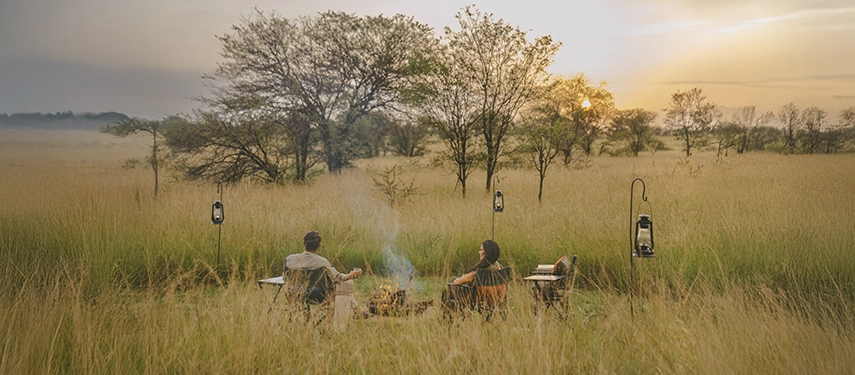 A peaceful sundowner scene at Nyasi Tented Camp, with lanterns glowing among long grass as the sun sets over the northern Serengeti.