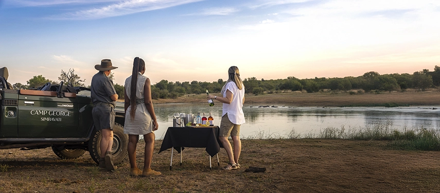 Guests gather for sundowners beside a river after an afternoon game drive at Simbavati Camp George in the Timbavati wilderness.