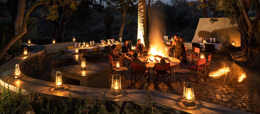 Guests gather around a lantern-lit boma fire for dinner at Simbavati Camp George, enjoying an atmospheric evening under African skies.