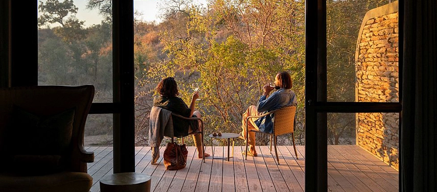 Two guests relax on a private deck at Simbavati Camp George, enjoying sunset views and quiet moments overlooking the bush.