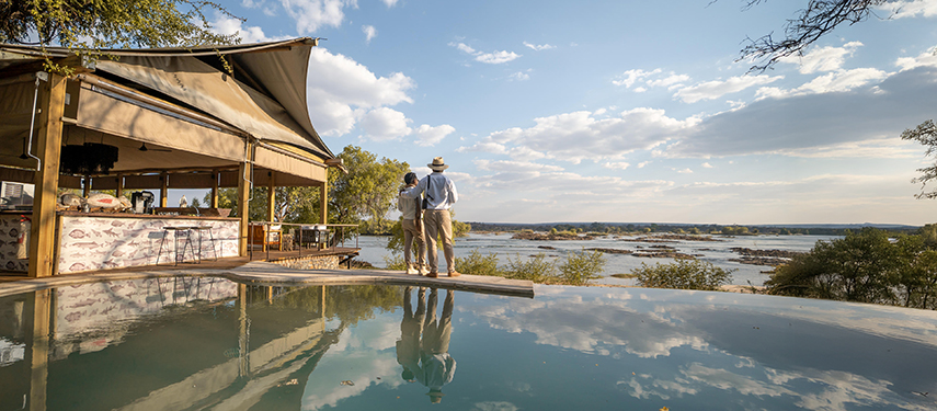 Couple standing beside the infinity pool at Toka Leya with sweeping river views