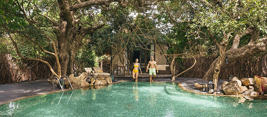 Couple entering a luxurious pool surrounded by trees at Uga Jungle Beach resort