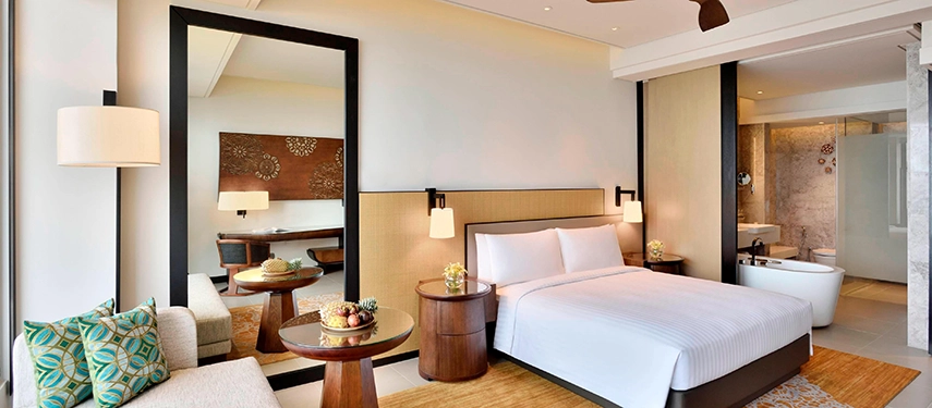 A stylish guestroom at Weligama Bay Marriott Resort & Spa featuring a modern seating area, warm natural tones, and a spacious open-plan bathroom.