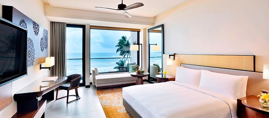 A serene oceanfront guestroom at Weligama Bay Marriott Resort & Spa with large picture windows framing the turquoise sea.