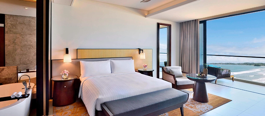 An elegantly appointed suite at Weligama Bay Marriott Resort & Spa featuring a plush bed, freestanding bathtub, and panoramic views across the Indian Ocean.