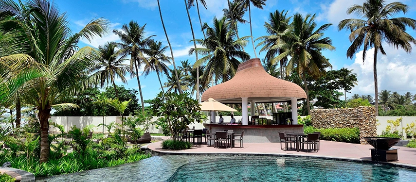 A poolside bar at Weligama Bay Marriott Resort & Spa surrounded by tropical gardens and tall palms, offering shaded seating beside the water.