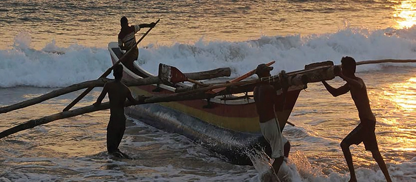 Local fishermen push a traditional wooden boat into the surf at sunrise near Weligama Bay Marriott Resort & Spa.