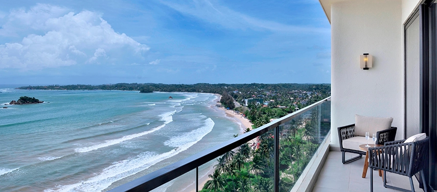 A serene balcony setup at Weligama Bay Marriott Resort & Spa overlooking clear blue waters and the palm-lined coast.