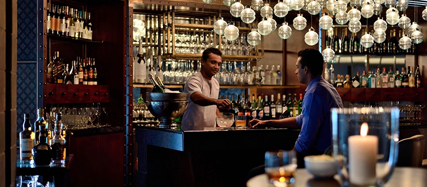 A bartender pours a drink for a guest at the intimate, warmly lit bar at Weligama Bay Marriott Resort & Spa.