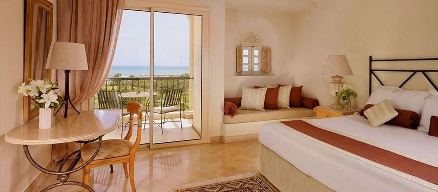 Bright sea-facing hotel room with balcony, king-sized bed, and soft neutral tones overlooking the Mediterranean.