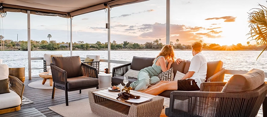 Couple relaxing on a riverside deck watching sunset over the Zambezi near Insika Lodge, Victoria Falls.