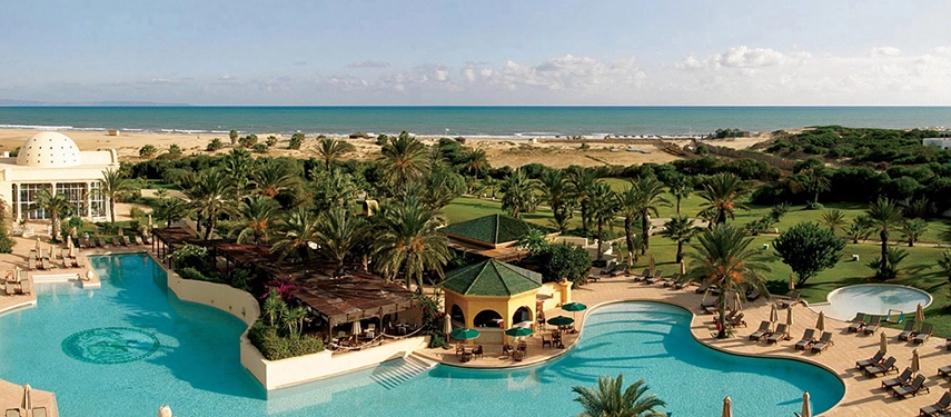 Expansive aerial view of The Residence Tunis in Tunisia with lagoon-style pools, palm trees, and panoramic Mediterranean Sea views.