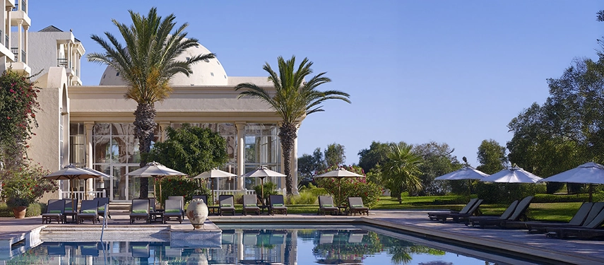 Elegant poolside at a luxury Tunisian resort with loungers, umbrellas, and a domed building surrounded by palms and gardens.
