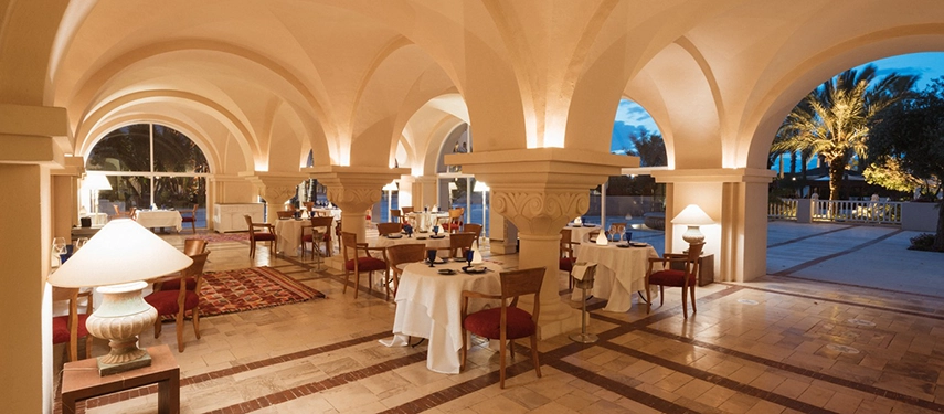 Romantic evening dining setup beneath vaulted arches at The Residence Tunis restaurant with candlelit tables.