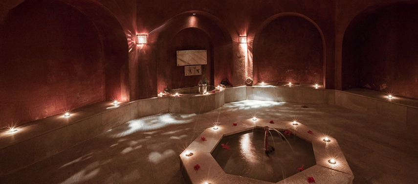 Romantic candle-lit hammam with arched alcoves and a central stone plunge pool, offering a serene spa experience in Tunisia.