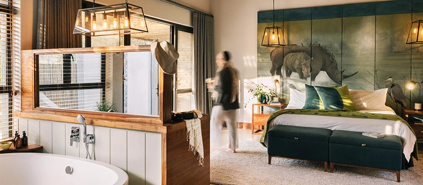 A spacious en suite bedroom at Simbavati Camp George combines classic safari styling with soft textures and hand-painted wildlife artwork.