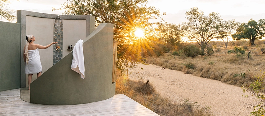 An outdoor shower at Simbavati Camp George looks out across bushveld at sunrise, blending privacy with a deep connection to nature.