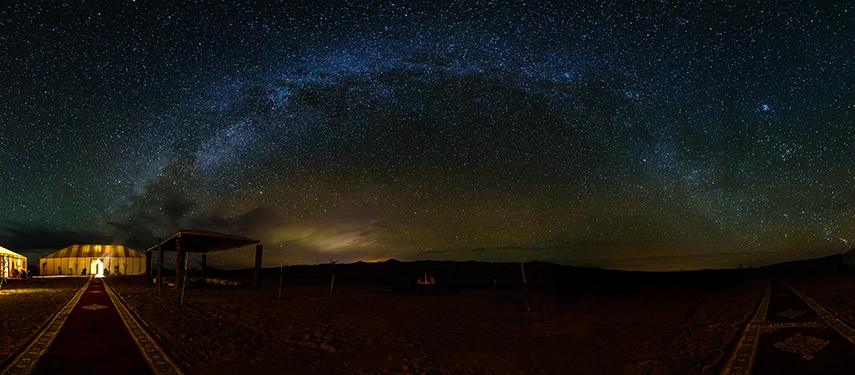 A wide desert night sky filled with stars arching over luxury tents at Auberge du Sud Luxury Desert Camp.