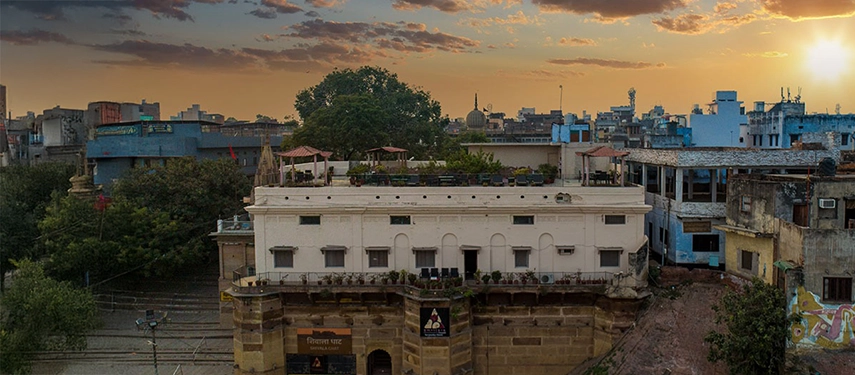 Exterior view of Amritara Suryauday Haveli at sunset with rooftop seating and surrounding city buildings.