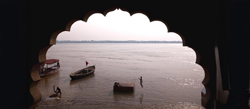 Scenic river view framed by an arched haveli window with boats and swimmers in the Ganges.