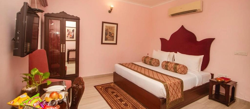 Elegant double room with pink walls, lotus-shaped headboard, and traditional Indian decor accents.