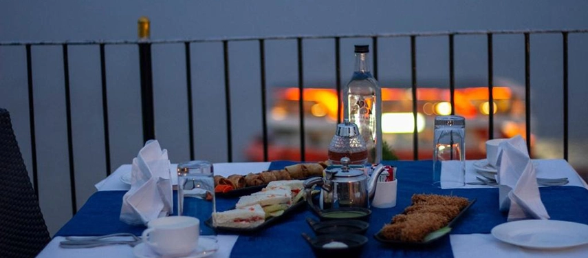 Close-up of a candlelit al fresco dinner table set with tea, snacks, and savoury dishes overlooking the river.