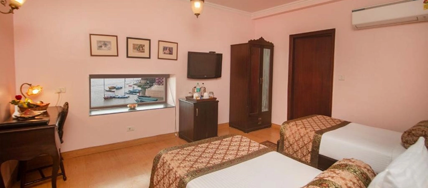 Twin-bed room with pastel pink walls, patterned bedding, and a window view of the Ganges River.