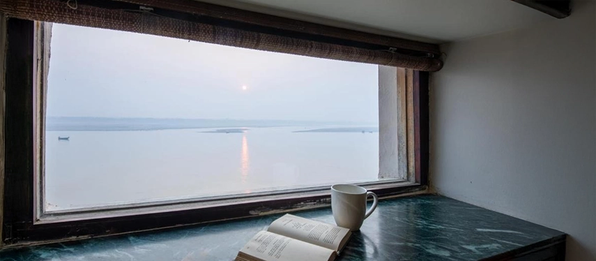 Window ledge with a coffee cup and open book, offering a tranquil view of sunrise over the Ganges.