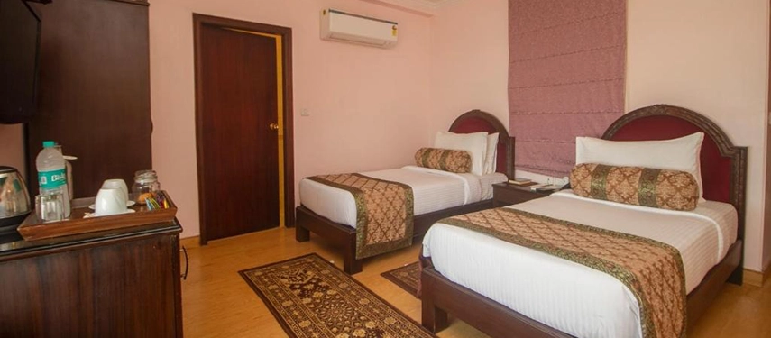 Twin-bed room with matching patterned bedding, pink accent wall, and wooden furnishings.