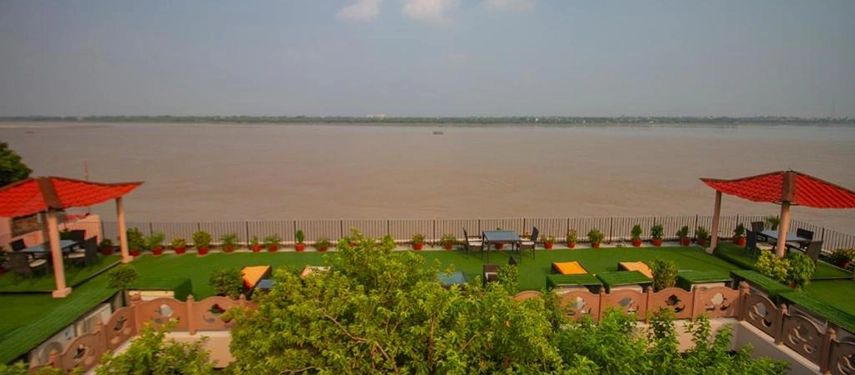 Rooftop terrace with shaded seating areas, green lawns, and uninterrupted views over the Ganges.