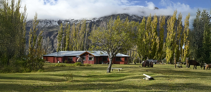 Exterior view of Estancia El Cóndor surrounded by tall poplar trees with mountains in the background.
