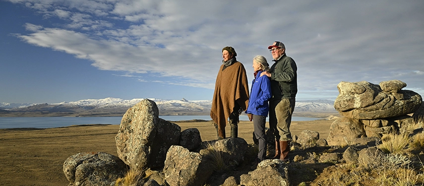 Three people standing on a rocky hillside overlooking Lago San Martín and the Patagonian mountains.