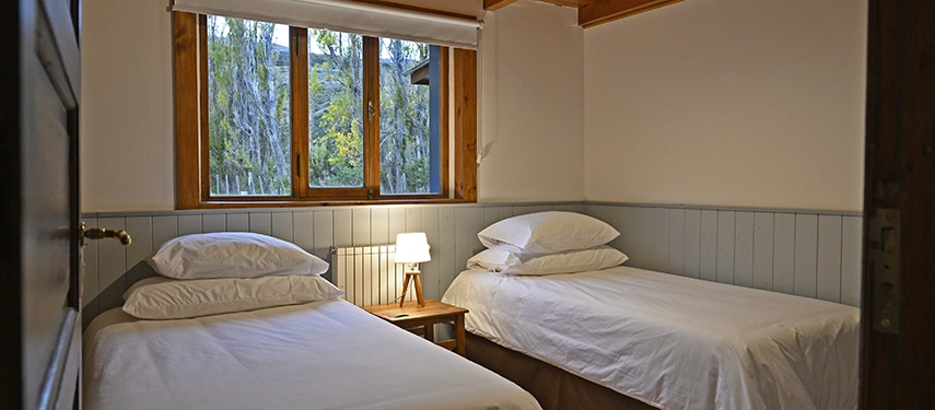 Twin-bedded guest room with wooden floors and large window views at Estancia El Cóndor.