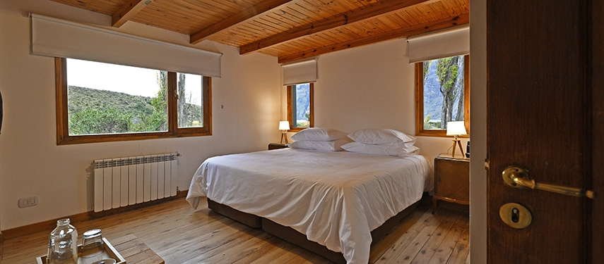 Double room with a king-size bed, wooden ceiling, and scenic window views at Estancia El Cóndor.