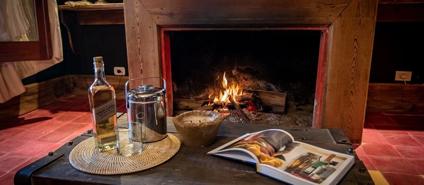 Cosy fireplace scene with a bottle of whisky, glass, and open book at Estancia Don Joaquín.