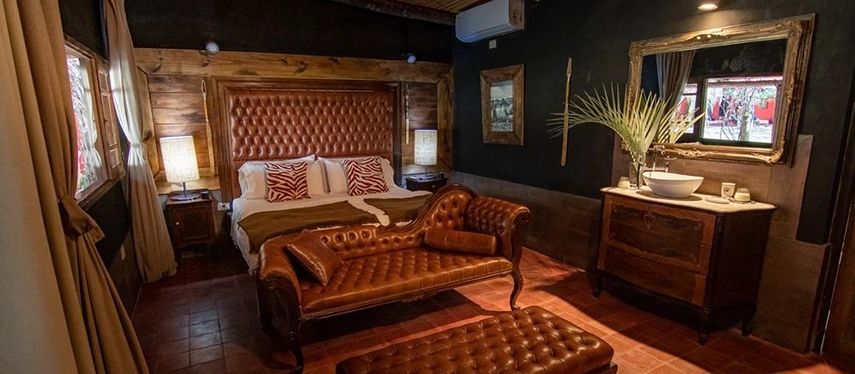 Luxurious suite with rich wooden tones, leather sofa, and large framed mirror at Estancia Don Joaquín.