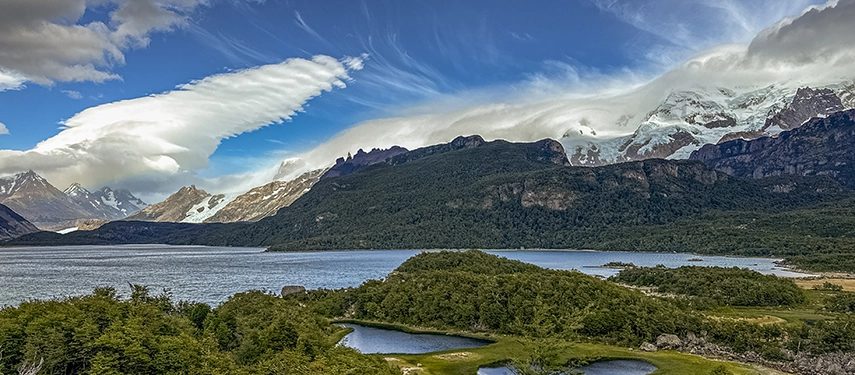 A dramatic panorama of lakes, forests and towering snow-capped peaks unfolds beneath sculpted Patagonian clouds.