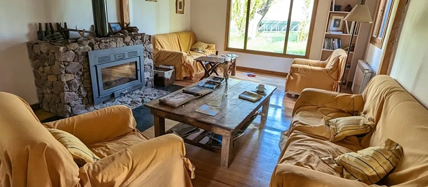 Cozy lounge with yellow slip-covered sofas, a stone fireplace, and views of the estancia grounds.