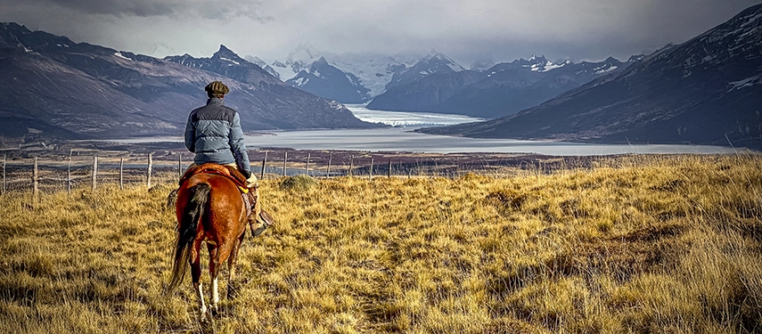 A rider moves quietly across golden steppe towards a distant glacier framed by brooding Patagonian mountains.