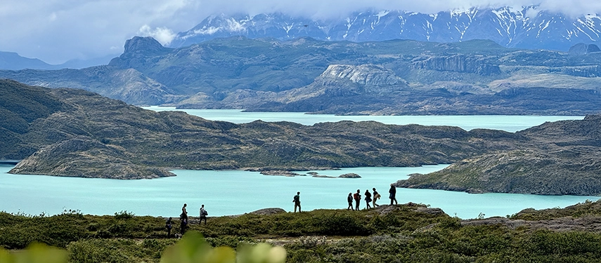 Group of hikers walking along a ridge with panoramic views of turquoise lakes and jagged peaks.