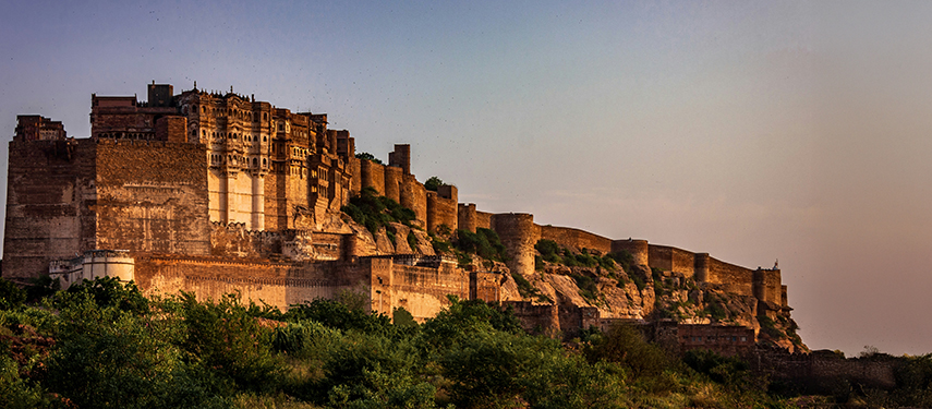 Majestic Mehrangarh Fort rising above the desert landscape at sunset.