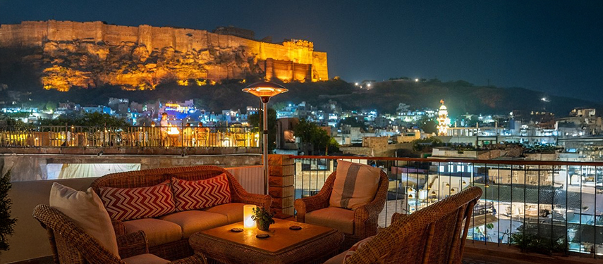 Rooftop lounge at The Stepwell House with illuminated Mehrangarh Fort in the background.
