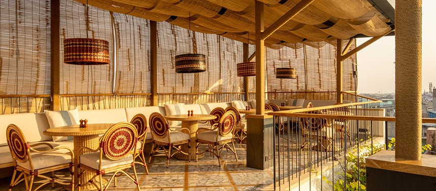 Sunlit rooftop dining area at The Stepwell House featuring woven decor and city views.